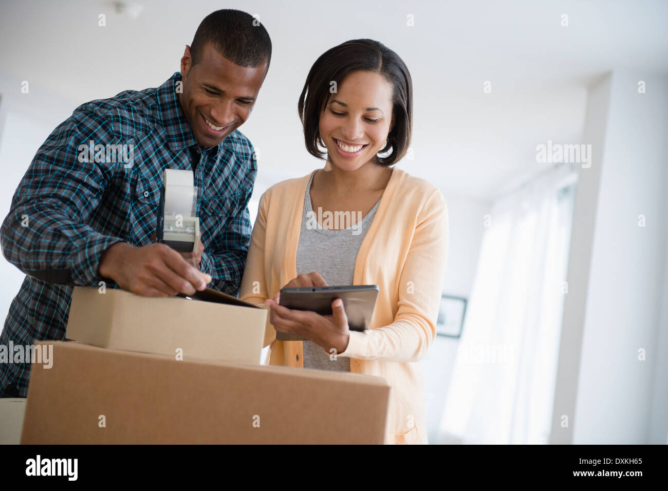 Couple with digital tablet taping up moving boxes Stock Photo