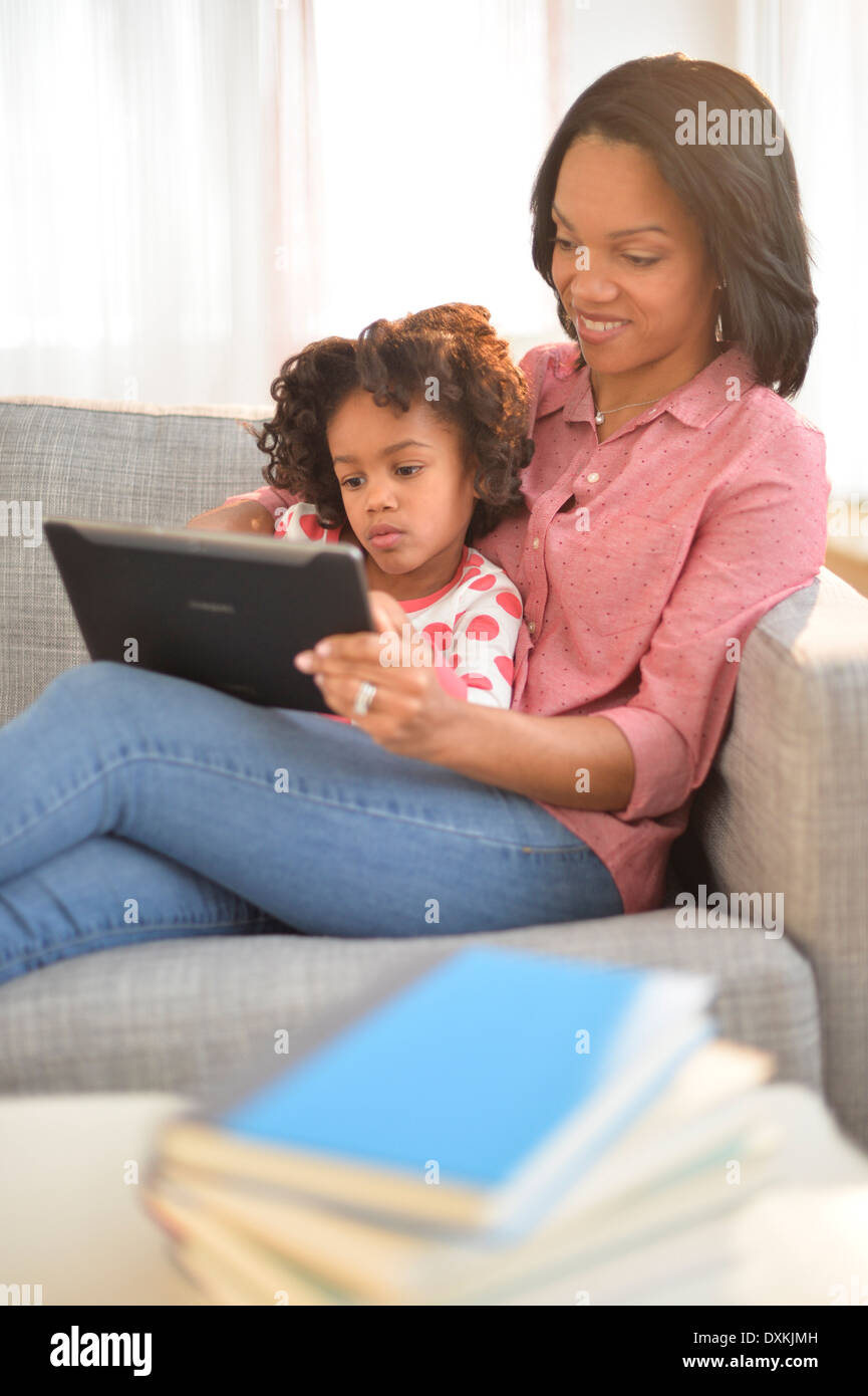Black mother and daughter using digital tablet on sofa Stock Photo
