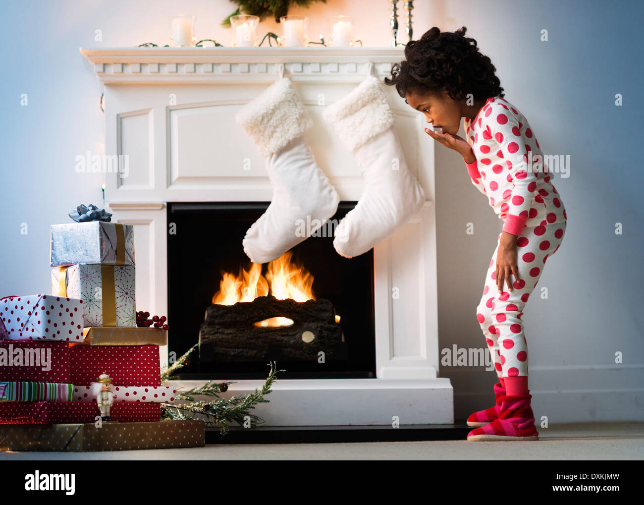 Surprised Black girl in pajamas looking down at Christmas gifts Stock Photo