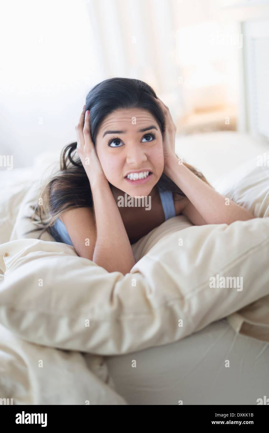 Frustrated Hispanic woman covering ears in bed Stock Photo