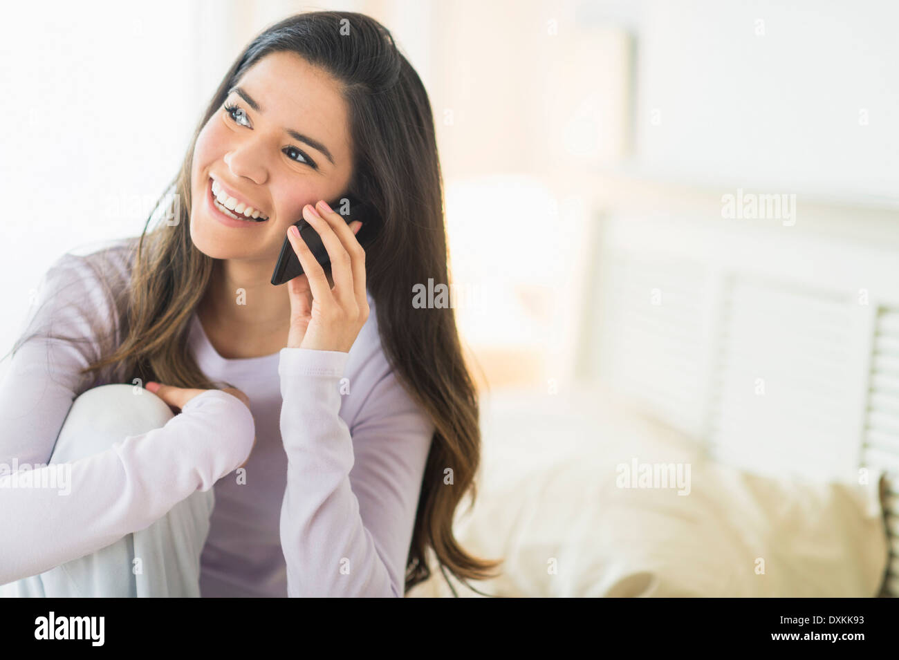 Happy Hispanic woman talking on cell phone in bed Stock Photo - Alamy