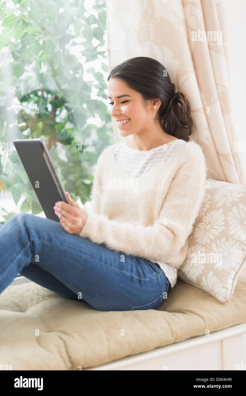 Hispanic woman using digital tablet at window seat Stock Photo
