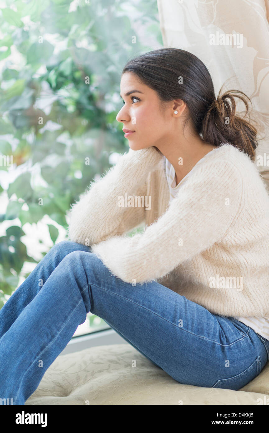 Pensive Hispanic woman looking out window Stock Photo