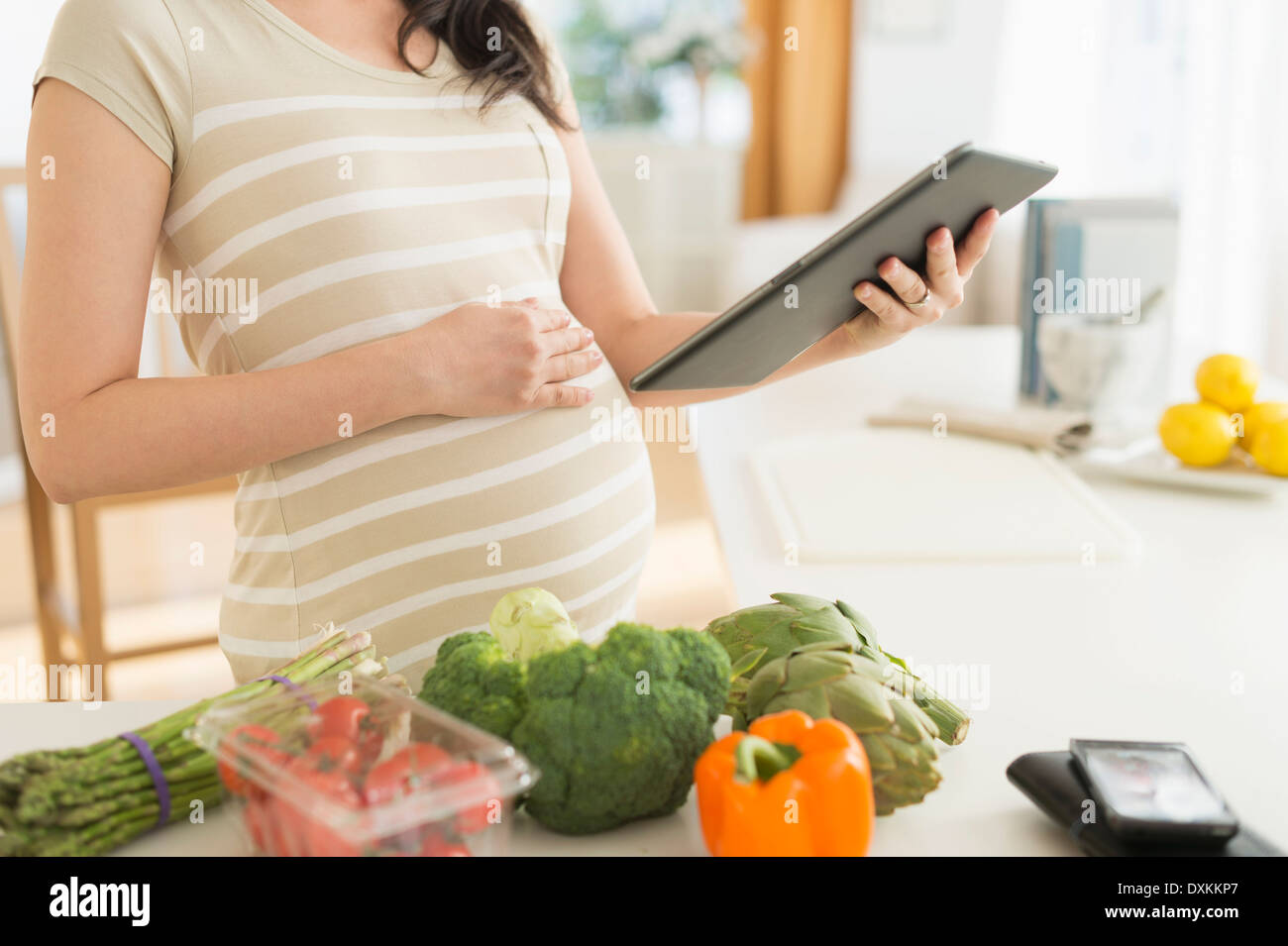 Pregnant Japanese woman using digital tablet in kitchen Stock Photo