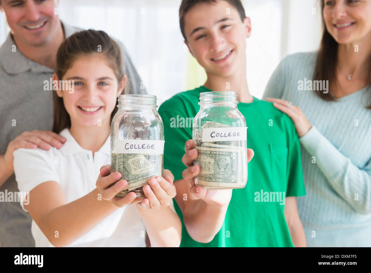 Proud Caucasian parents watching children with college savings jars Stock Photo