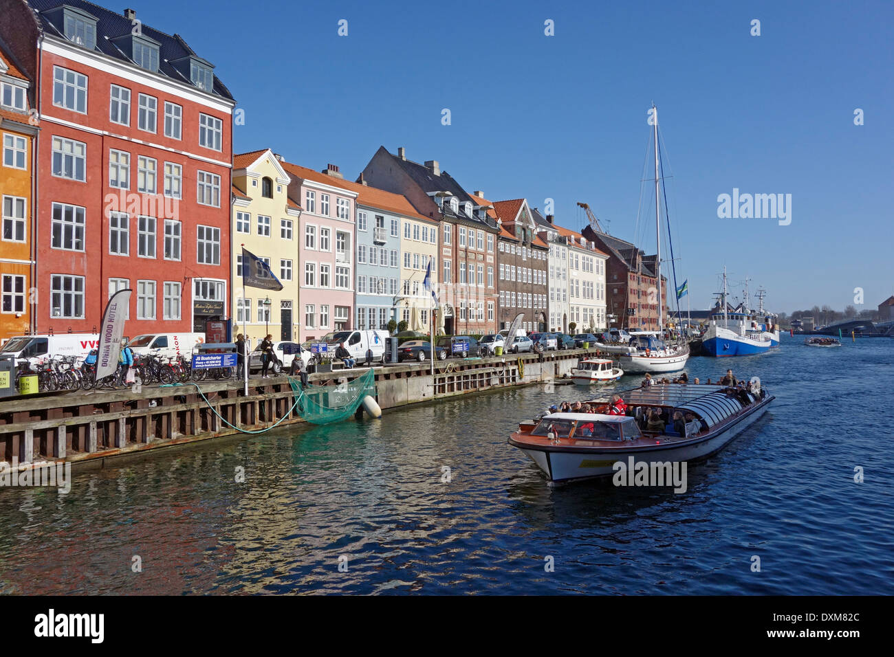 Colourful Nyhavn in Copenhagen Denmark mid March with canal touring boat arriving back from a tour round the harbour Stock Photo