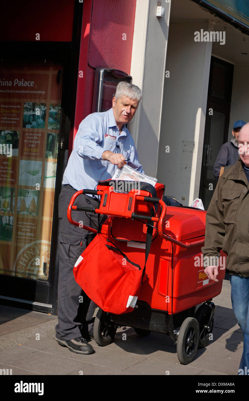 Postman on his round delivering letters & parcels using a 'high capacity' trolley (replacing the old fashioned bicycle) Stock Photo