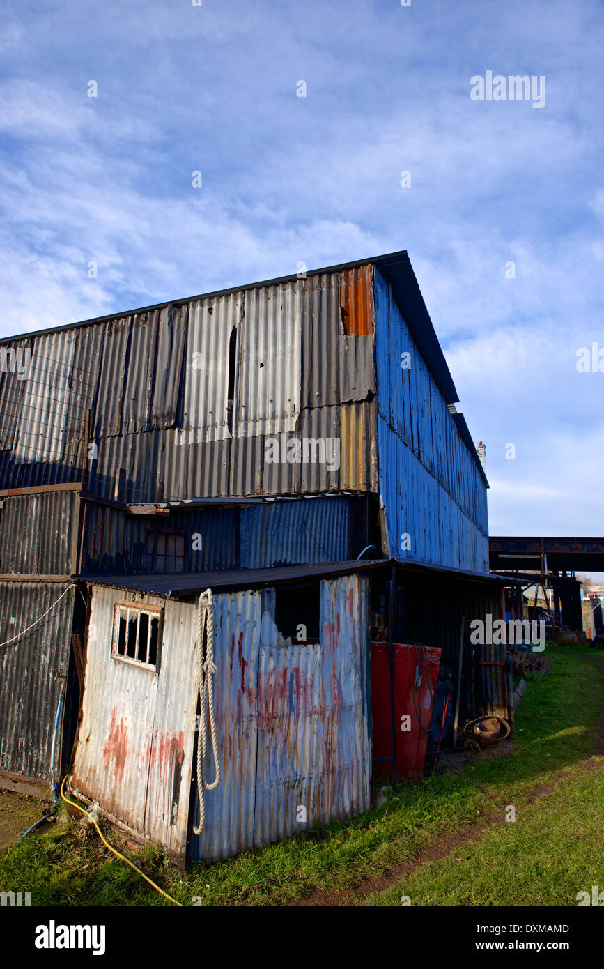 A rundown industrial building made of corrugated metal sheets, some of which are rusting. Industrial decline concept Stock Photo