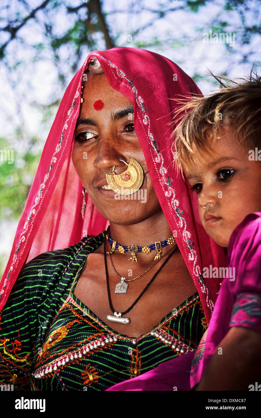 Indian woman wearing gold jewellery and pink headscarf carrying a small child in a village near Jodhpur, India Stock Photo