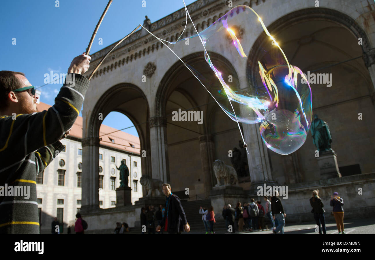 Munich, Germany. 27th Mar, 2014. A street artist blows a large soap bubble on Odeonsplatz outside of the Feldherrenhalle in Munich, Germany, 27 March 2014. Photo: PETER KNEFFEL/dpa/Alamy Live News Stock Photo