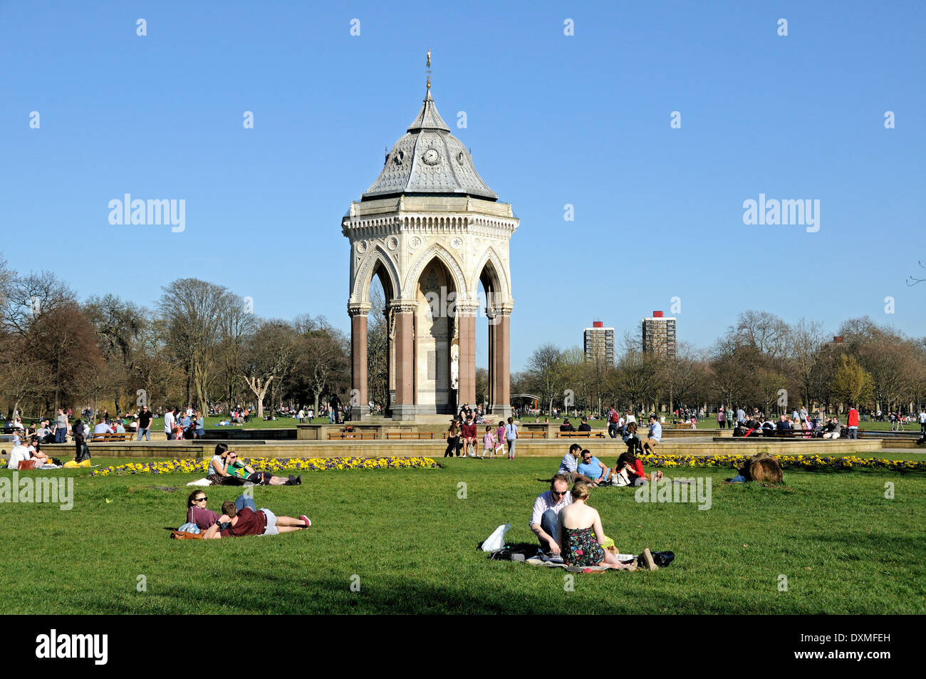 People sitting on the grass in Victoria Park with the Burdett-Coutts Memorial Drinking-Fountain Tower Hamlets London England UK Stock Photo