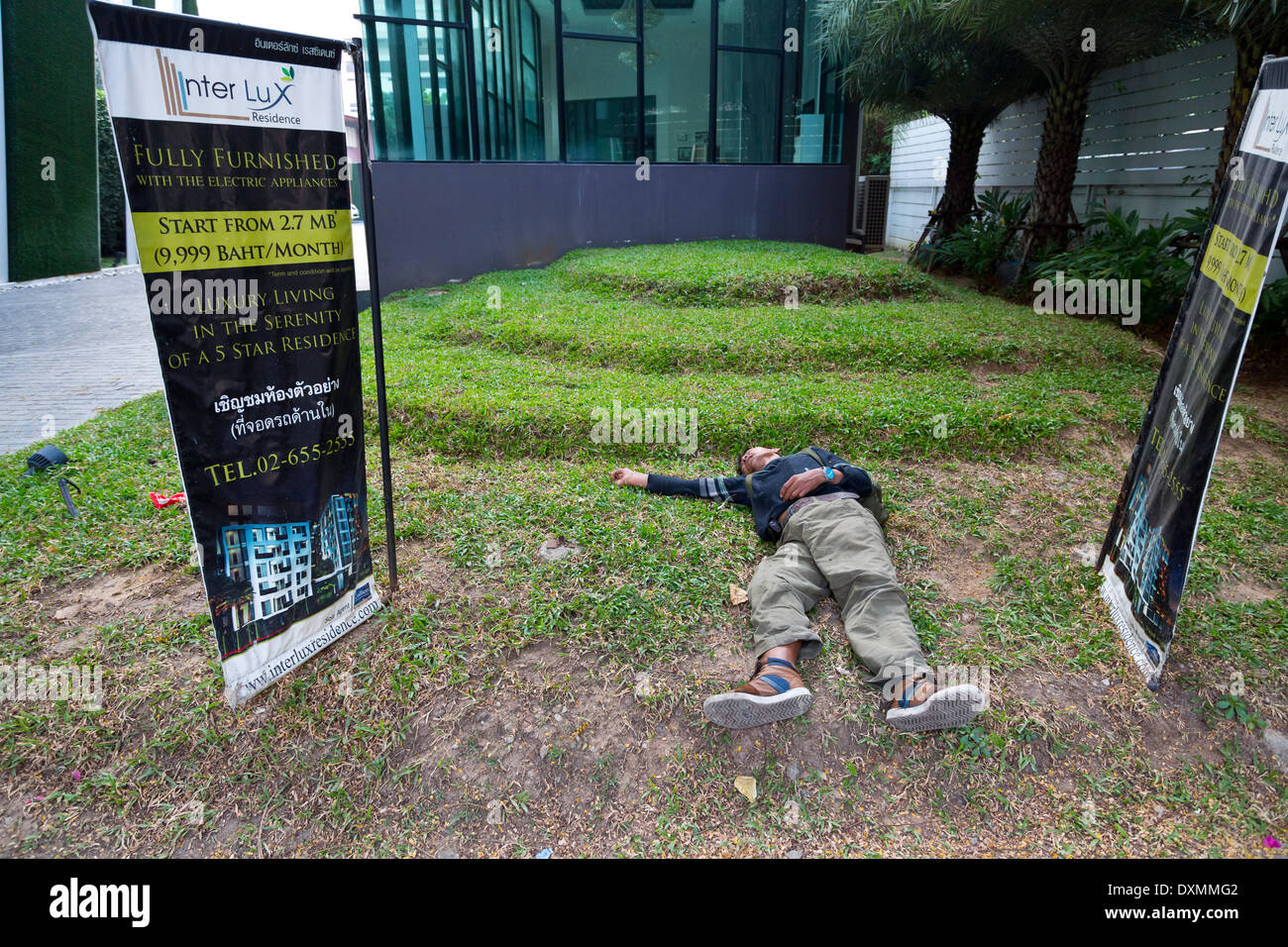 Homeless Man sleeping on the Lawn of a Luxury Compound in Bangkok, Thailand Stock Photo