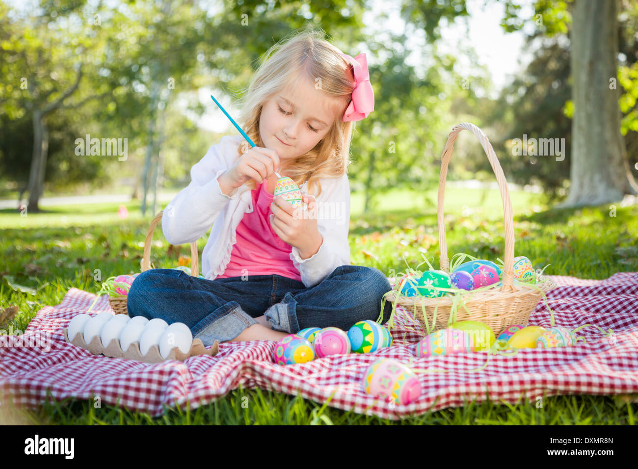 Cute Young Girl Happily Coloring Her Easter Eggs with Paint Brush in the Park. Stock Photo