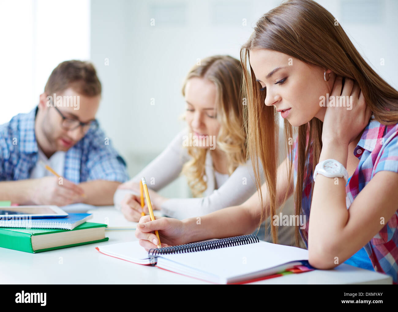 Smart girl carrying out written task with her groupmates on background Stock Photo