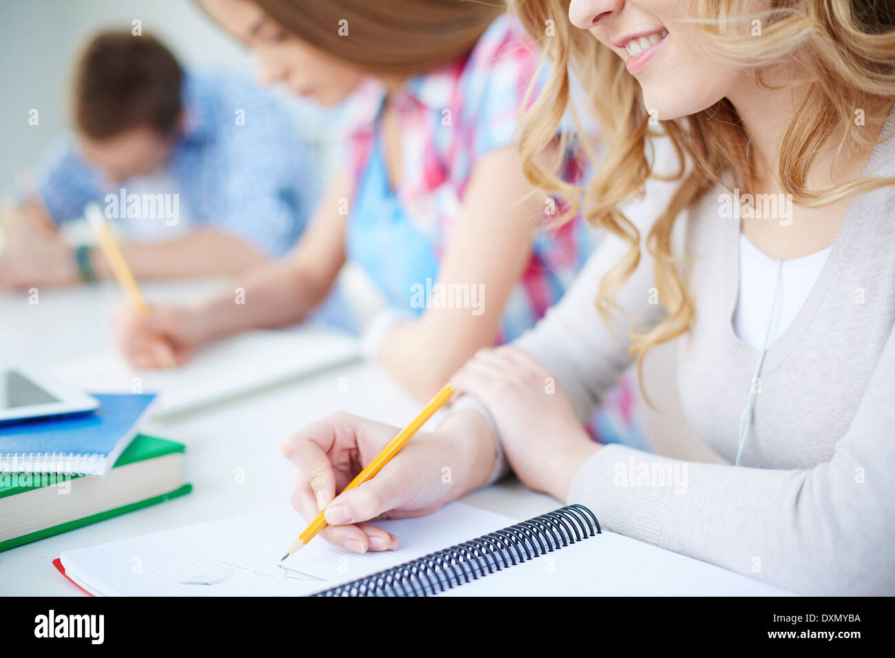 Smiling girl and her groupmates on background carrying out written task at lesson Stock Photo