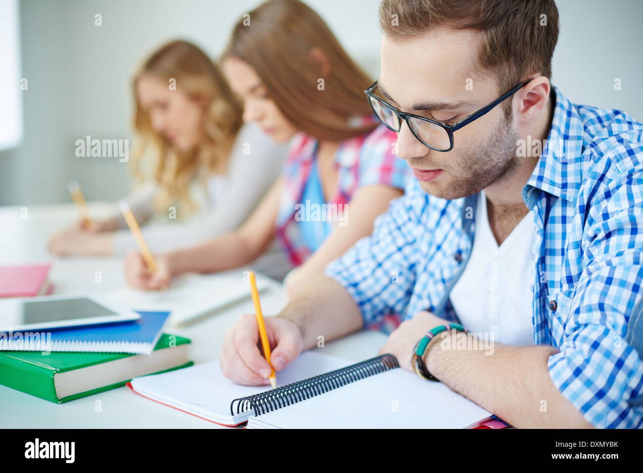 Serious guy and his groupmates on background carrying out written task at lesson Stock Photo