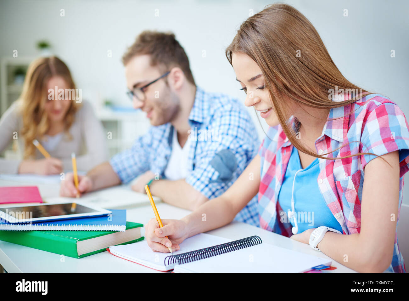 Smart girl and her groupmates on background carrying out written task at lesson Stock Photo