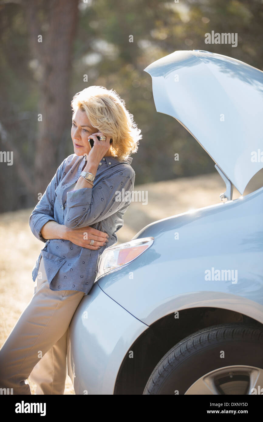 Woman talking on cell phone with automobile hood raised at roadside Stock Photo