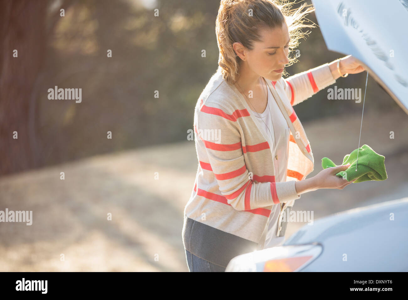 Woman checking oil under automobile hood at roadside Stock Photo