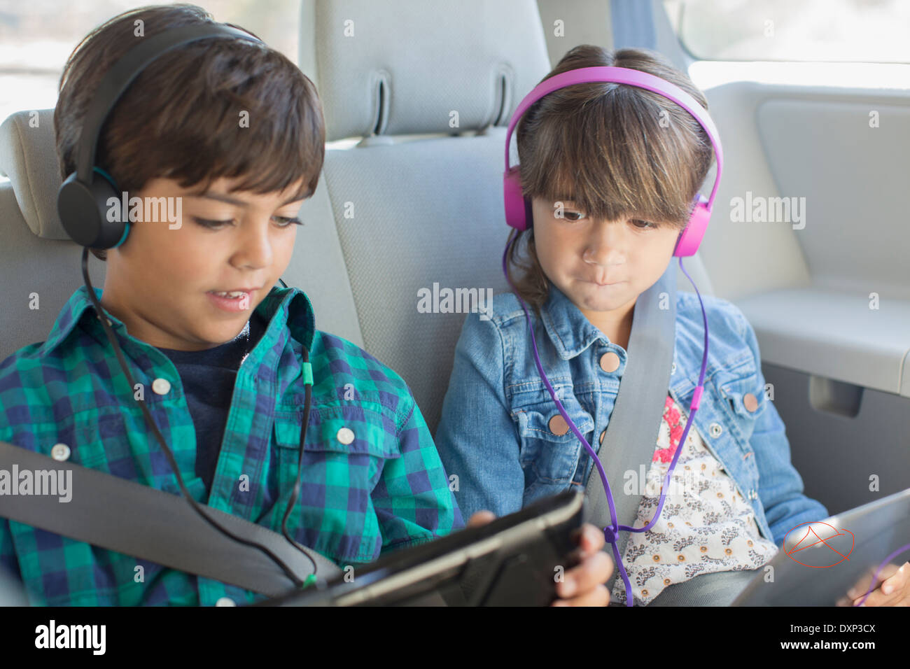 Brother and sister with headphones using digital tablets in back seat of car Stock Photo