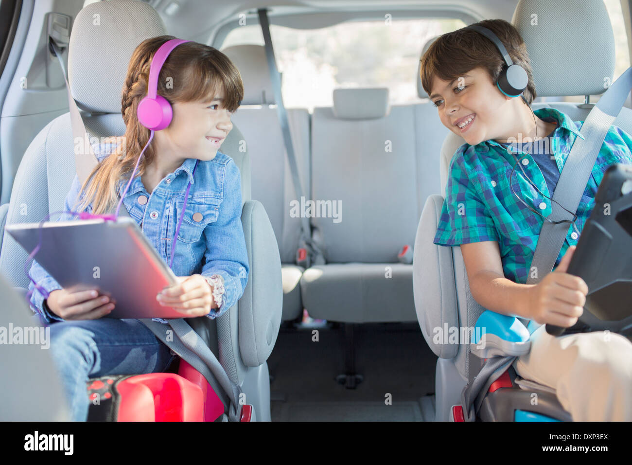 Happy brother and sister with headphones using digital tablets in back seat of car Stock Photo