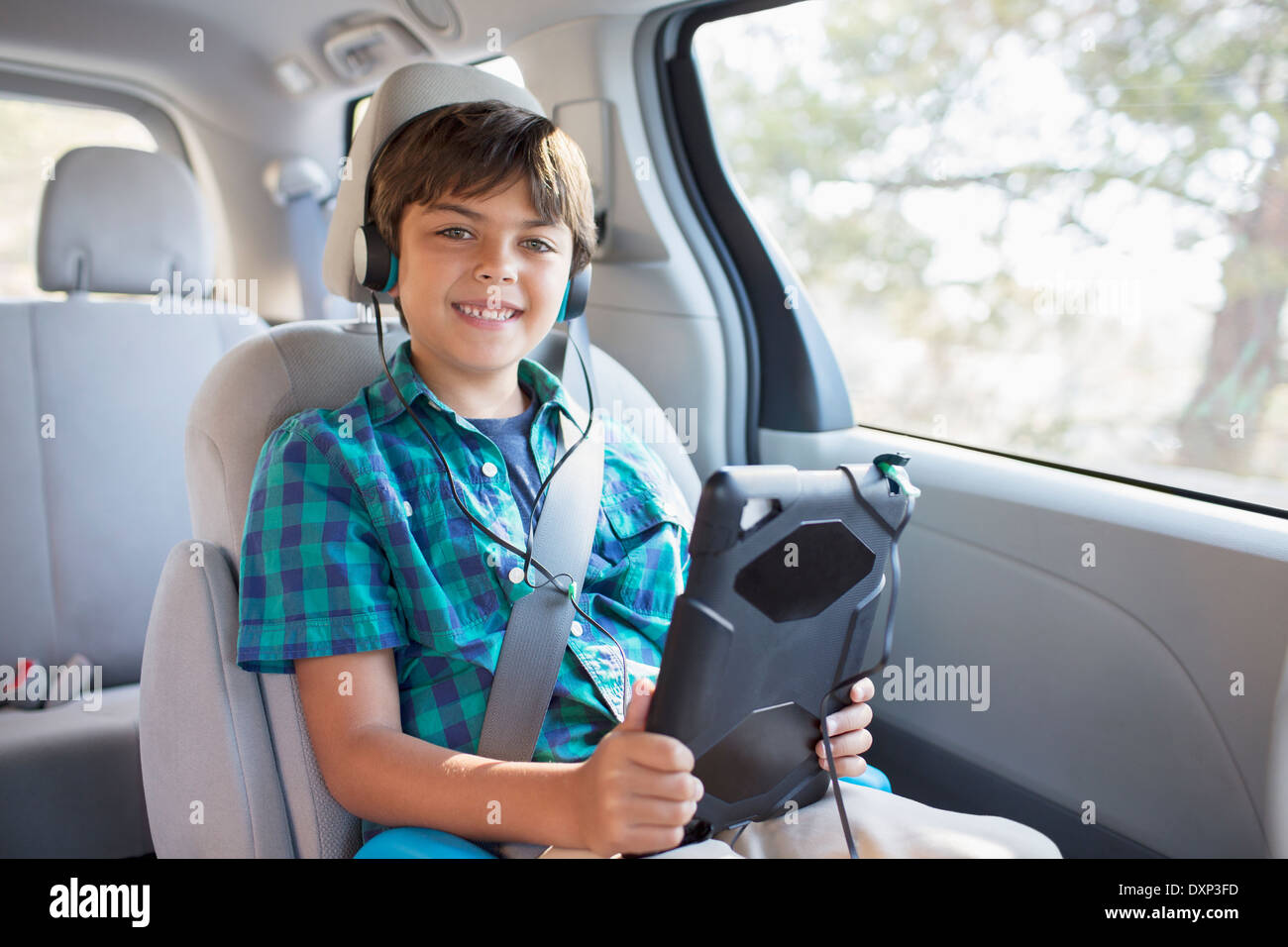 Portrait of happy boy with headphones using digital tablet in back seat of car Stock Photo