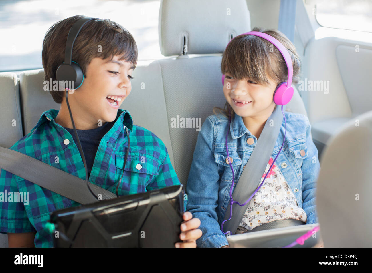 Happy brother and sister with headphones using digital tablets in back seat of car Stock Photo