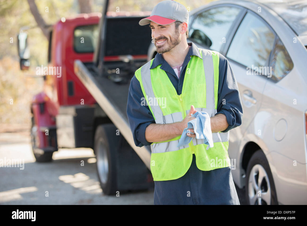 Roadside mechanic wiping hands with cloth next to tow truck Stock Photo