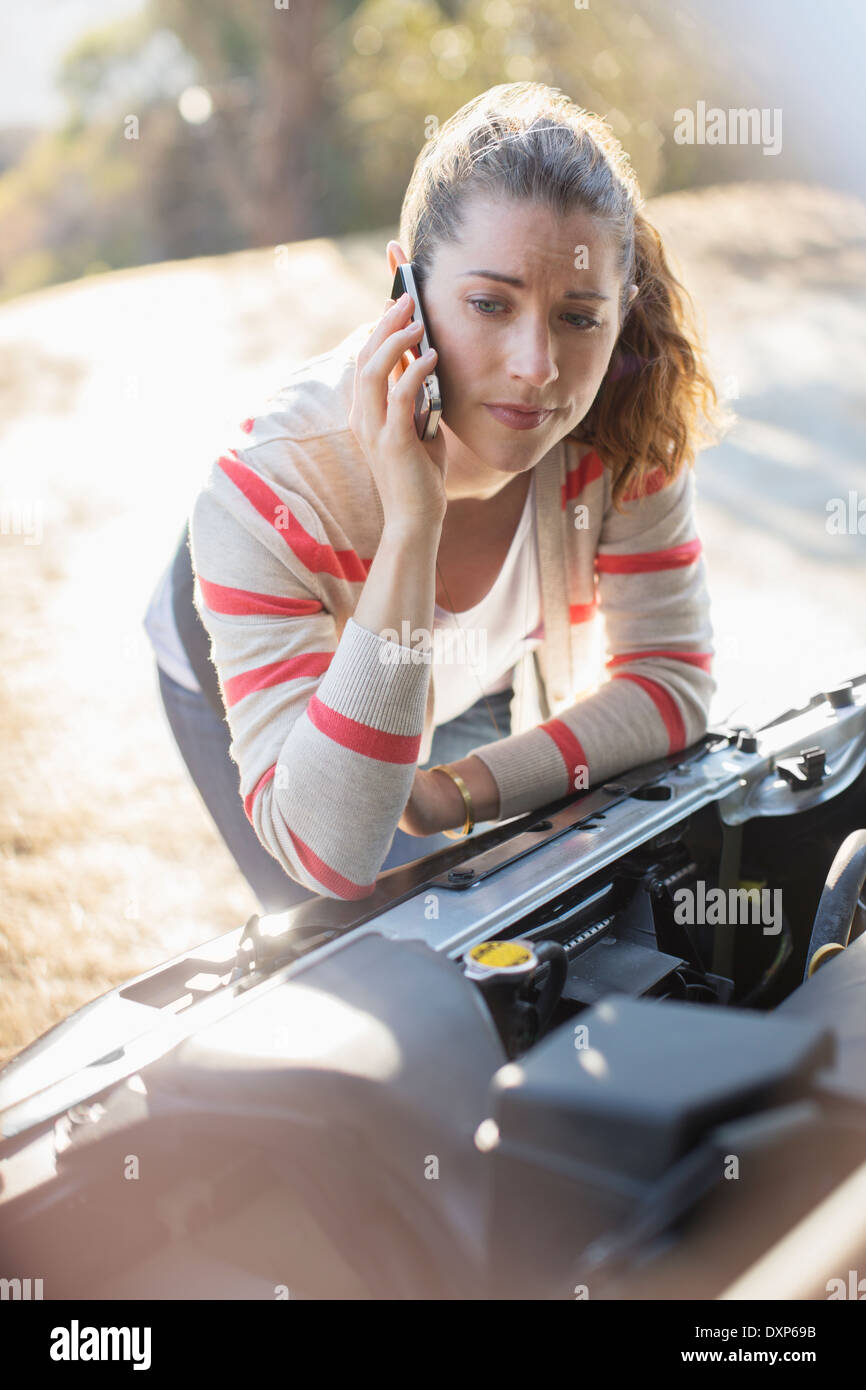 Frustrated woman talking on cell phone and looking at car engine Stock Photo
