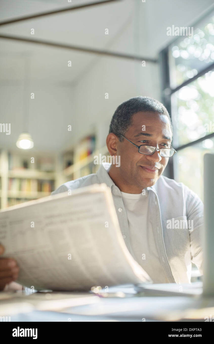 Senior man reading newspaper and using laptop Stock Photo