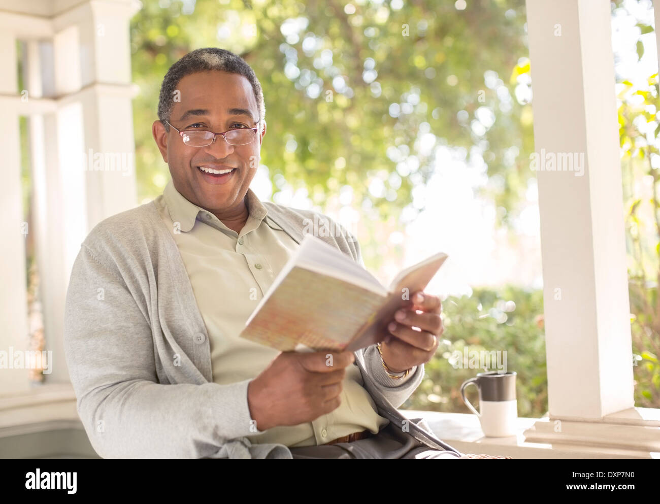 Portrait of smiling senior man reading book on porch Stock Photo
