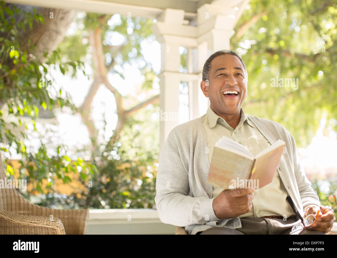 Laughing senior man reading book on porch Stock Photo