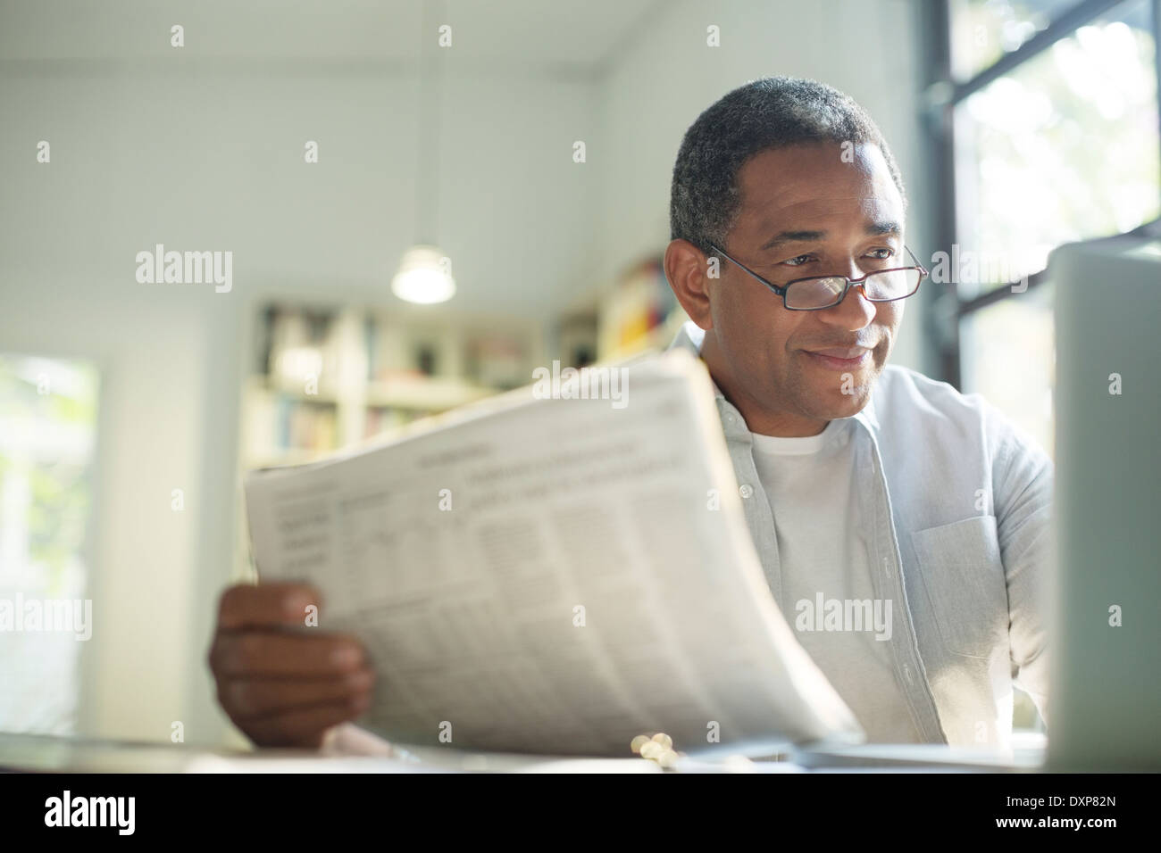 Senior man with newspaper using laptop Stock Photo
