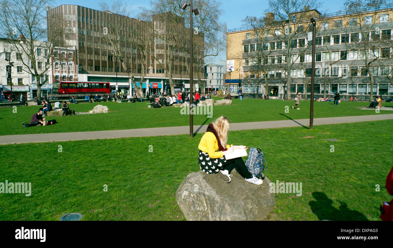 Woman in yellow jumper reading in Altab Ali Park on a sunny March day in Whitechapel East End London, UK KATHY DEWITT Stock Photo