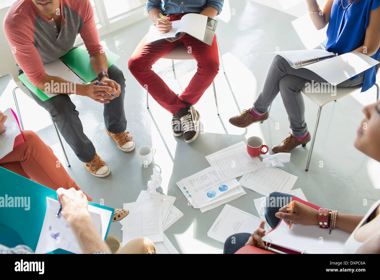 Creative business people meeting with coffee and paperwork in circle of chairs Stock Photo