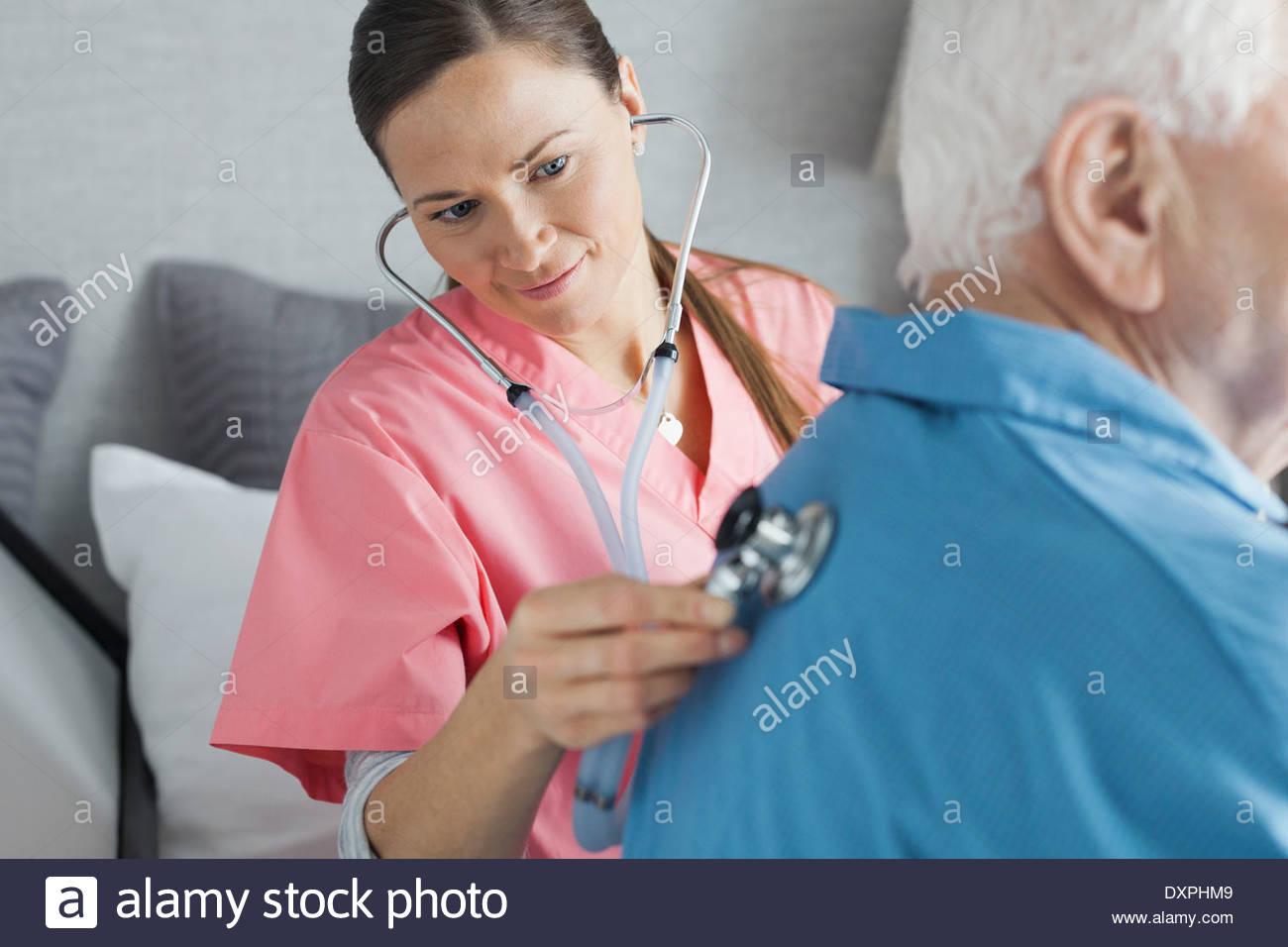 Home care nurse examining senior man with stethoscope Stock Photo