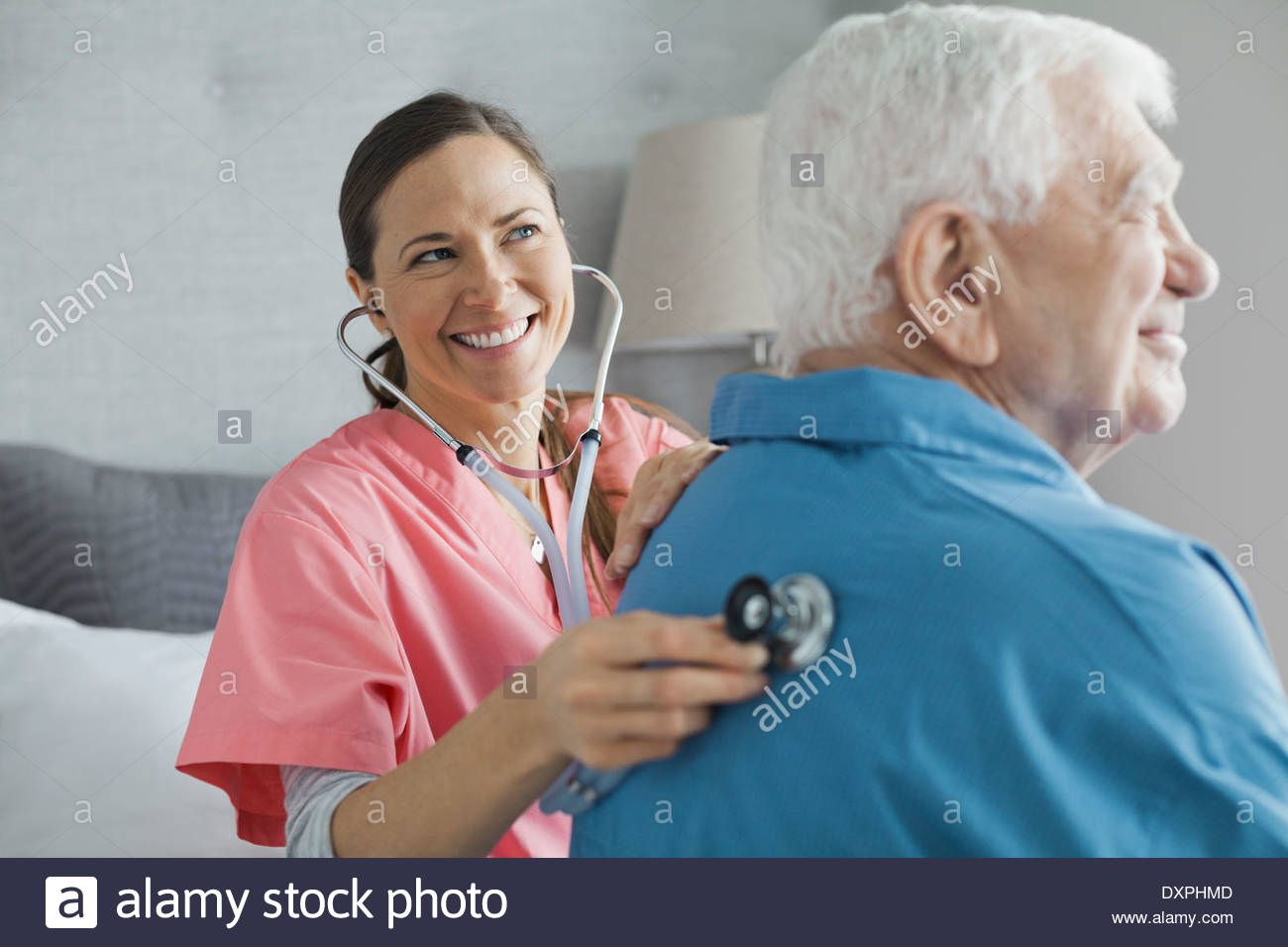 Home care nurse examining senior man with stethoscope Stock Photo