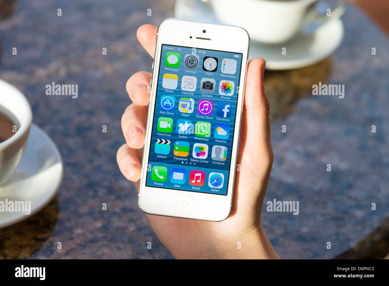 iOS 7 home screen of white Apple iPhone 5 in a cafe Stock Photo