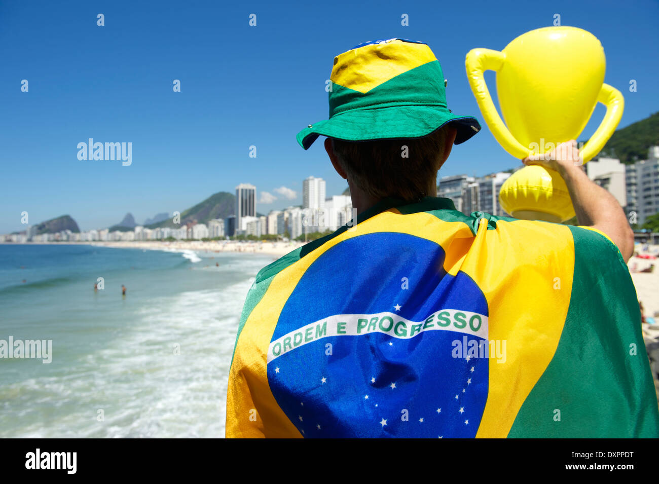 Proud Brazilian in flag regalia holding inflatable trophy above city skyline of Rio de Janeiro Brazil Stock Photo