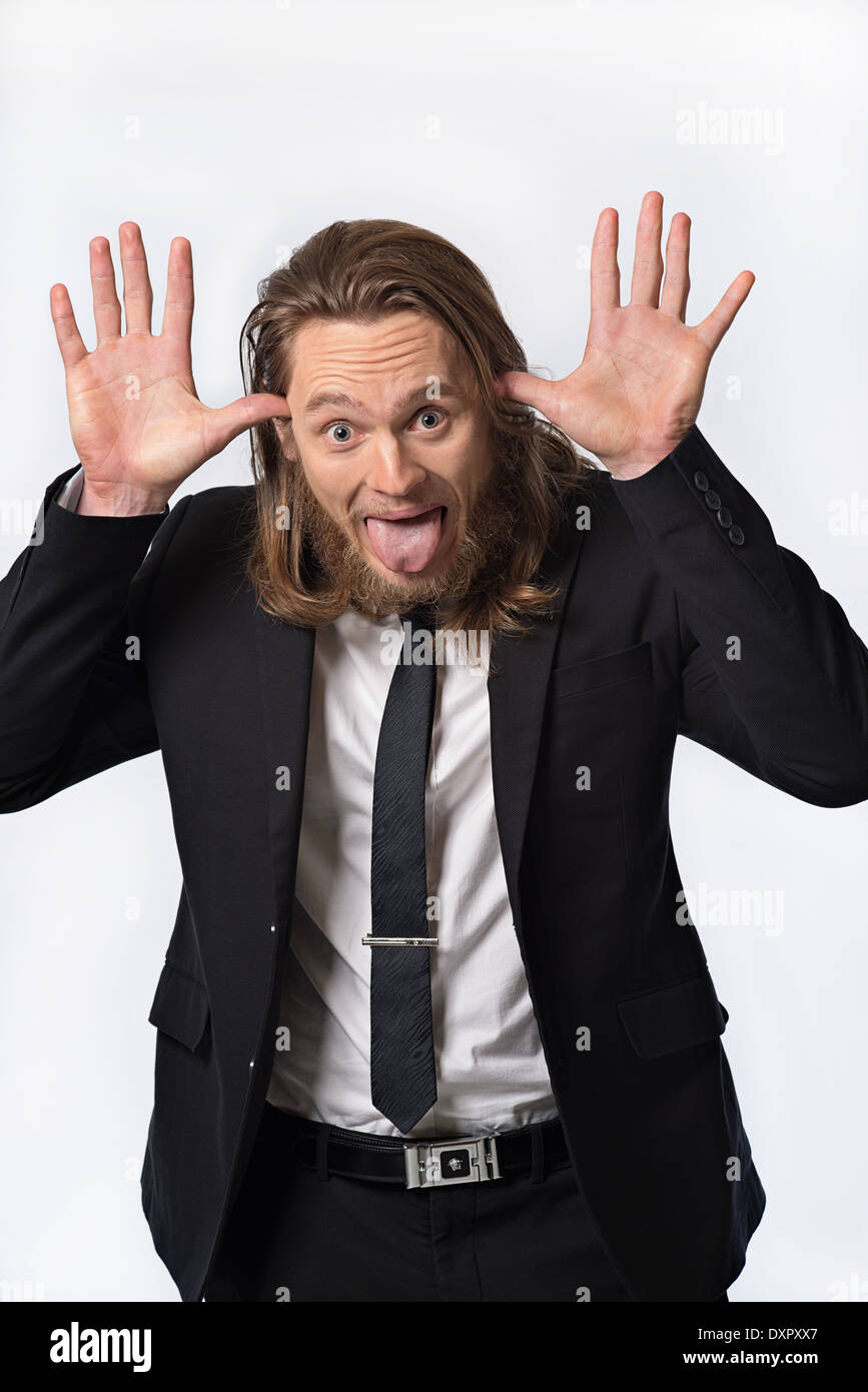 A bearded long hair man in suit with funny expression, sticking his tongue out, hands up. A humorous portrait concept Stock Photo
