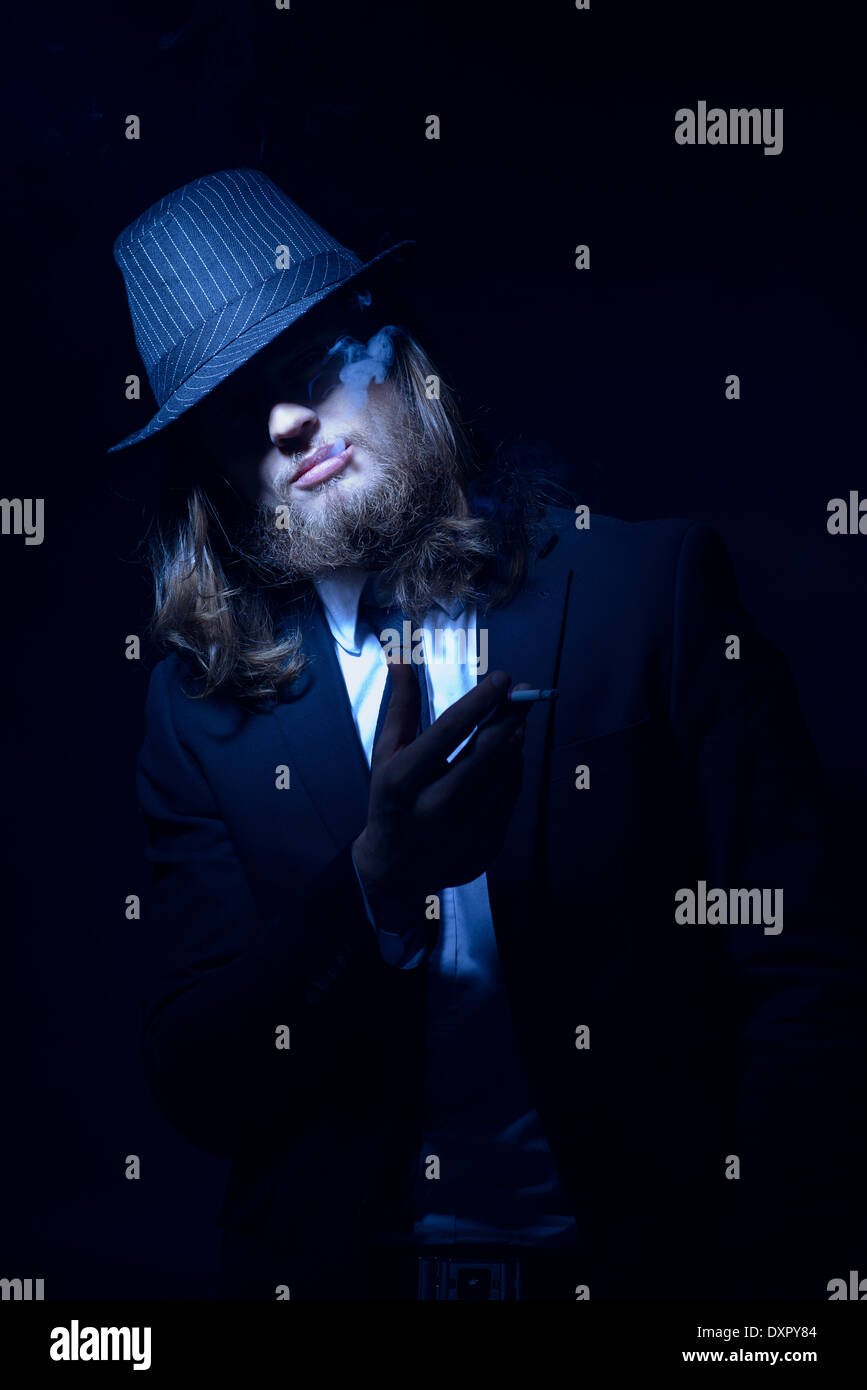 A bearded long hair man wearing a fedora hat and suit smoking Stock Photo