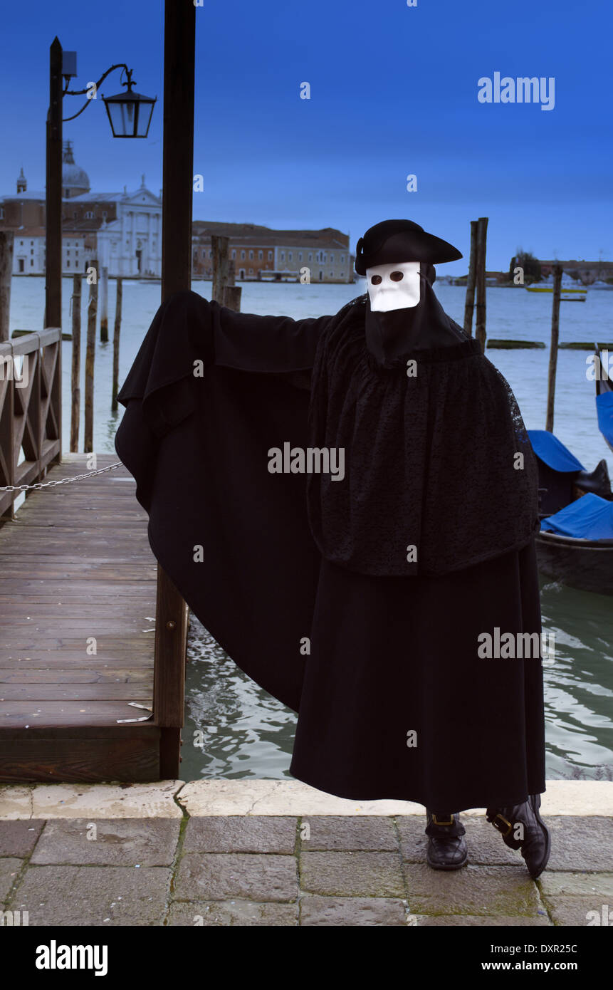 The man dressed in black cosume wearing white mask in Venice Stock Photo