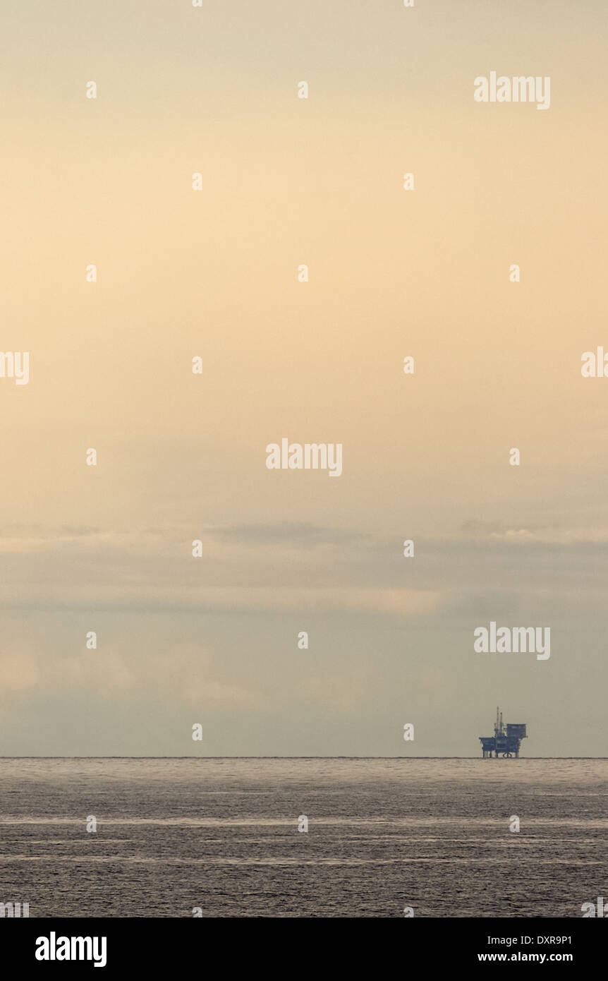 Single Scottish oil / gas rig far away on the horizon against a hazy evening sky. Stock Photo
