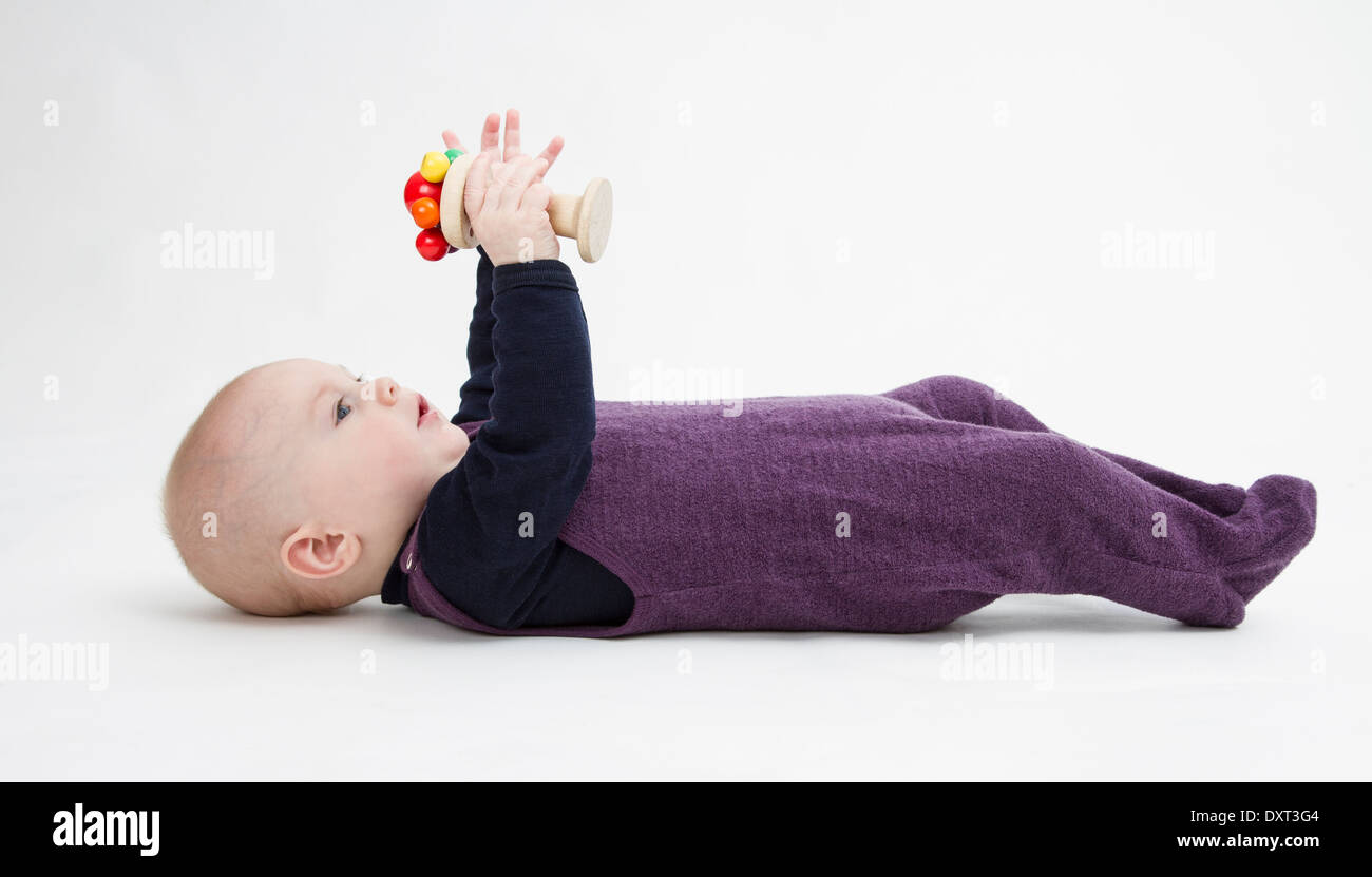 toddler lying on his back playing with wooden toy. grey background Stock Photo