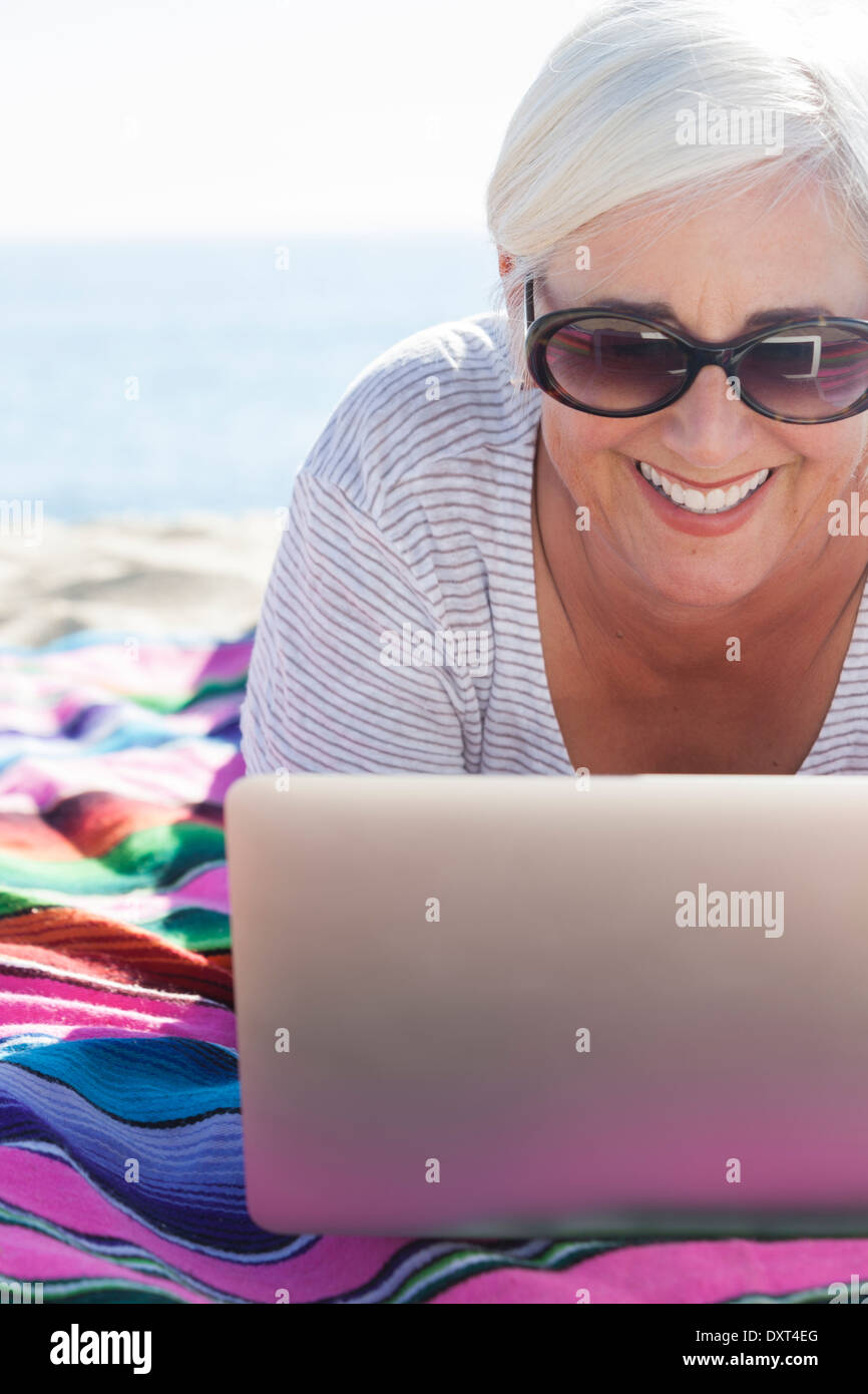 Happy woman using laptop on beach Stock Photo