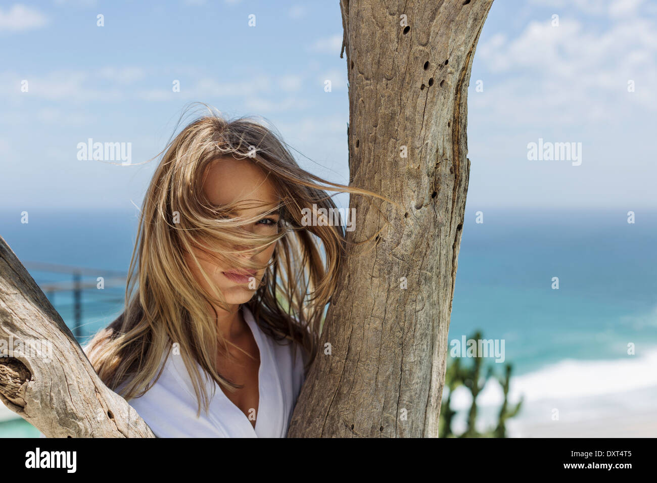 Wind blowing womanÍs hair in face behind tree trunk Stock Photo