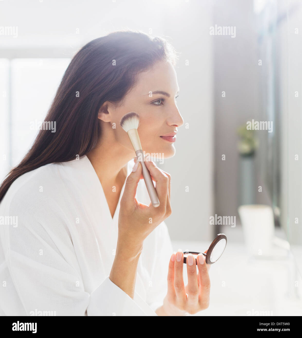 Woman in bathrobe applying makeup in bathroom Stock Photo
