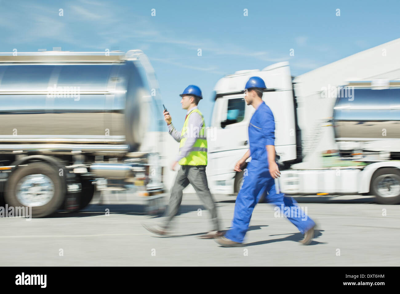 Workers walking past stainless steel milk tankers Stock Photo