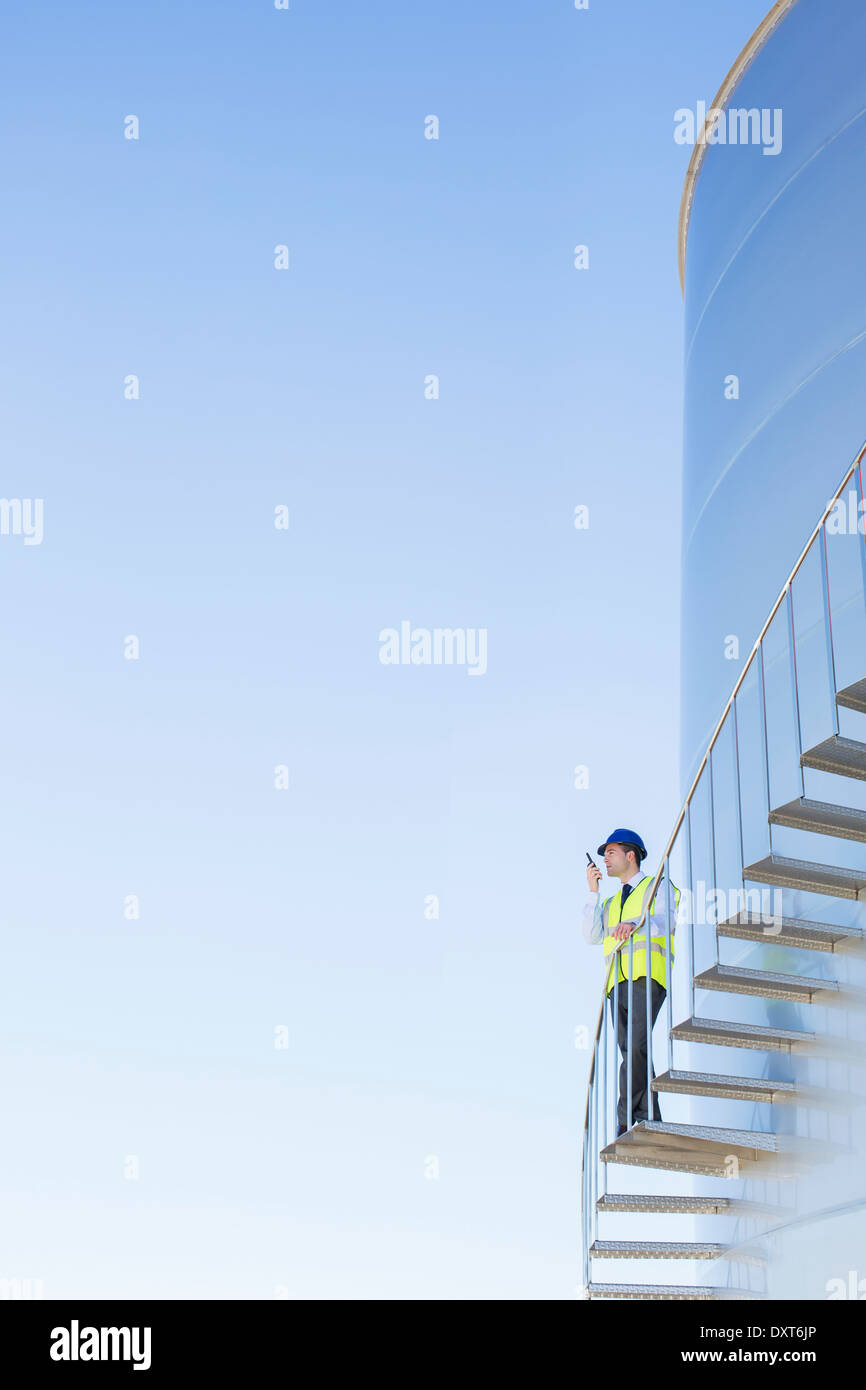 Worker using walkie-talkie on winding steps along silage storage tower Stock Photo