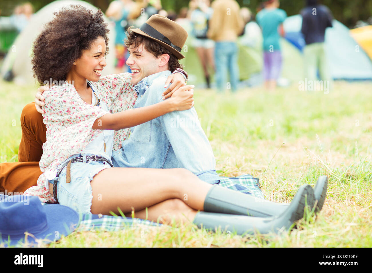 Couple hugging in grass outside tents at music festival Stock Photo